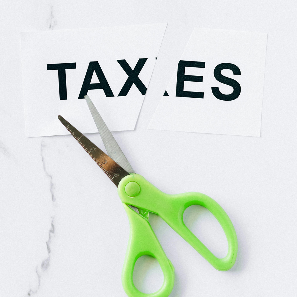 Photo of scissors and a cut piece of paper with the word taxes on it.