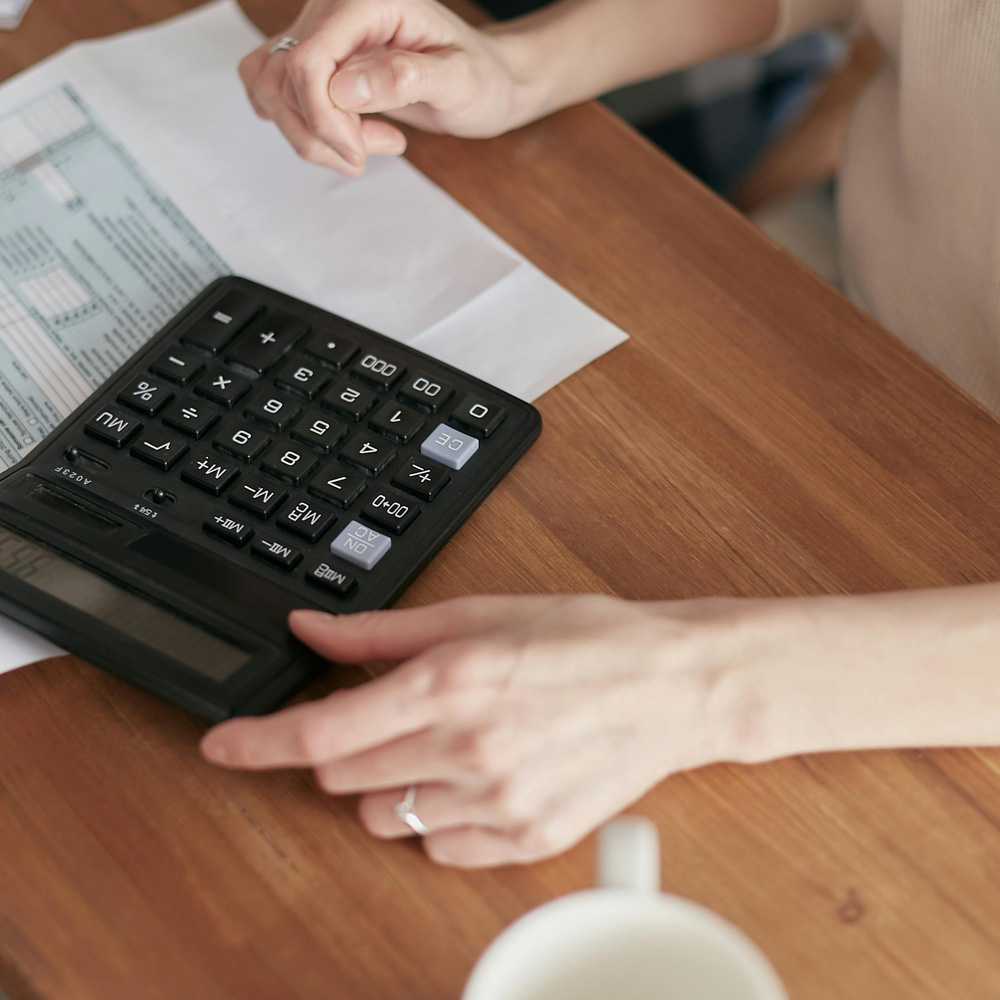 Photo of a woman's hands using a calculator in front of tax forms.